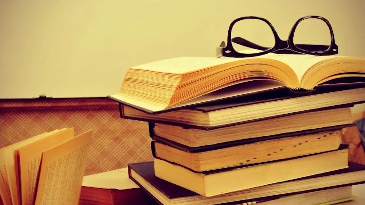 Stack of books piled into old suitcase with a pair of glasses on top